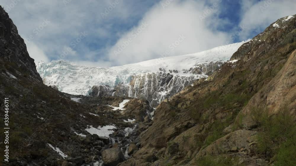 Aerial view of the Buarbreen glacier in the Folgefonna national glacier park near Odda, Norway. Clouds crawling atop the snow-covered mountain, sun rays piercing through, casting flares on the glacier