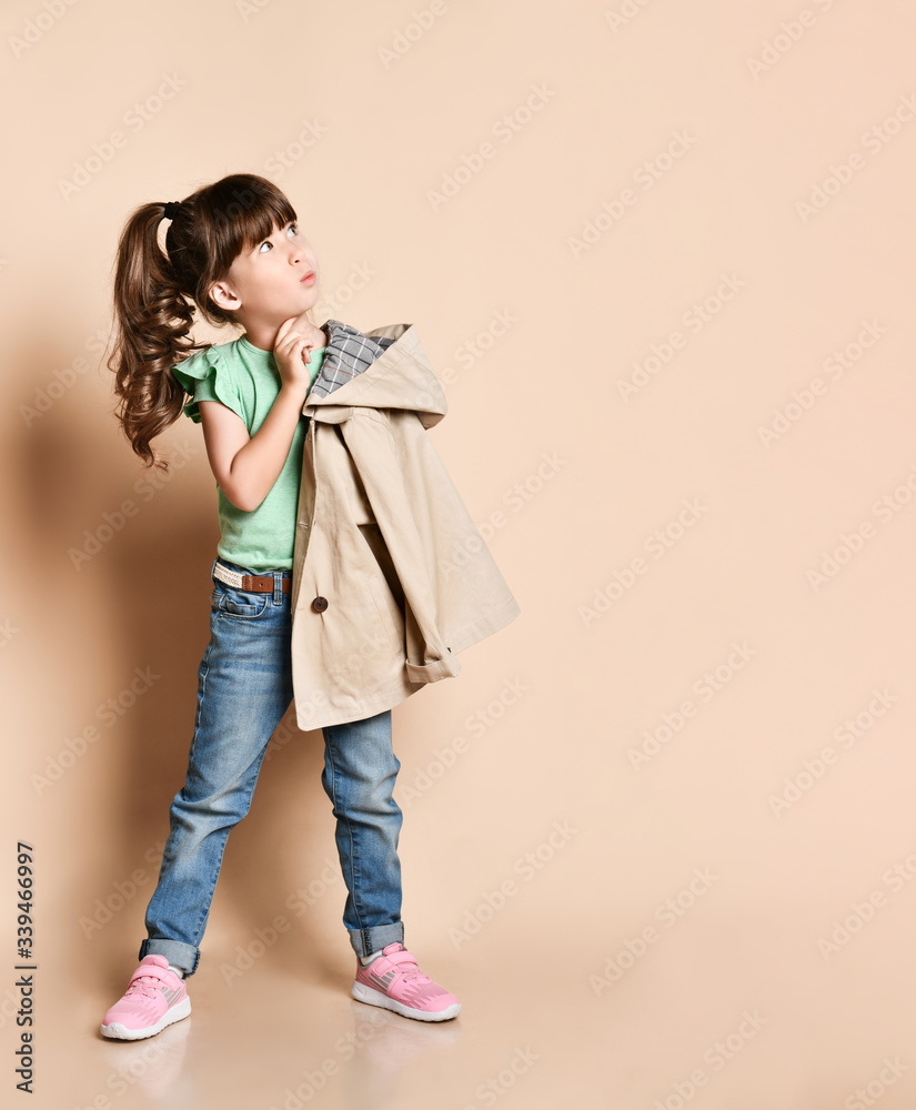 Cute girl posing standing in different poses, in jeans with belt, green t-shirt and beige coat and pink sneakers Cute girl posing standing in different poses, in jeans with belt, green t-shirt and beige coat and pink sneakers