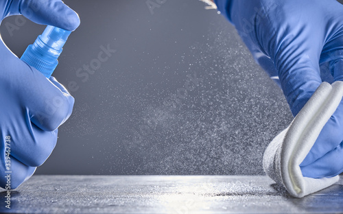 Hands in rubber gloves wipe the table with a disinfectant spray on a grey background. Disinfection of premises.