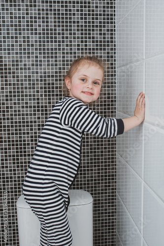 Cute girl in striped clothes washes a yellow rag on the wall. The child cleans at home. Household duties. Cute kid girl cleaning around. The idea of a child’s activity during quarantine