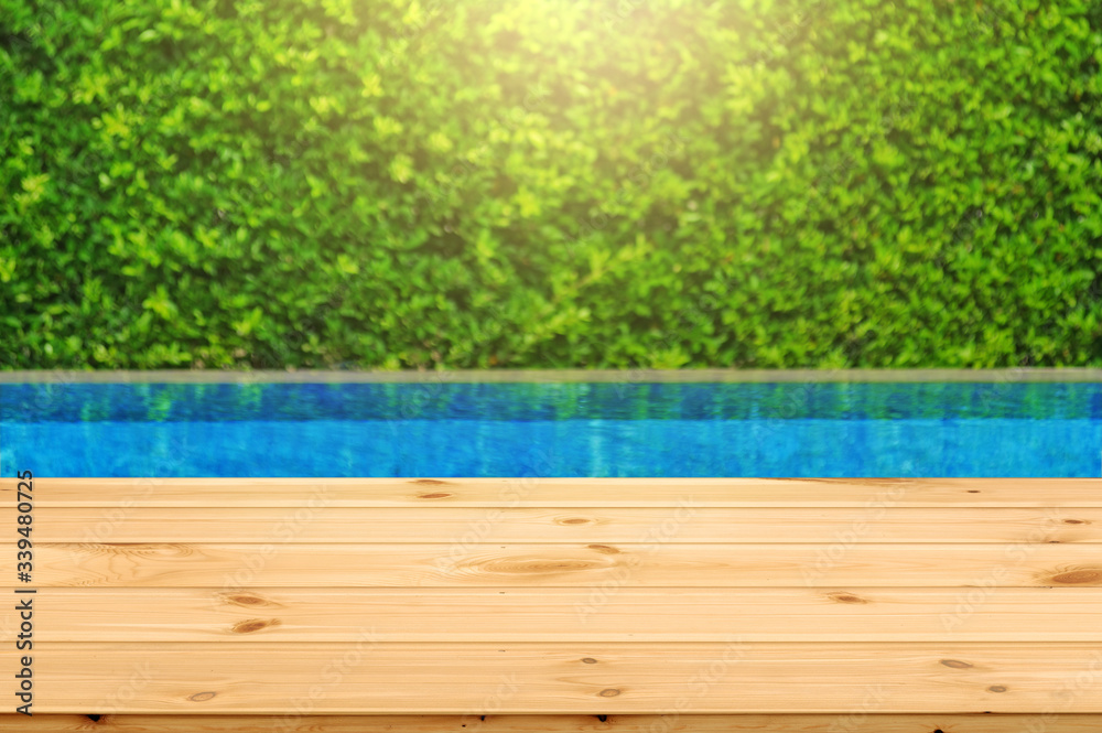 Wooden table in front with empty space for advertise display and blurred background of swimming pool and green garden