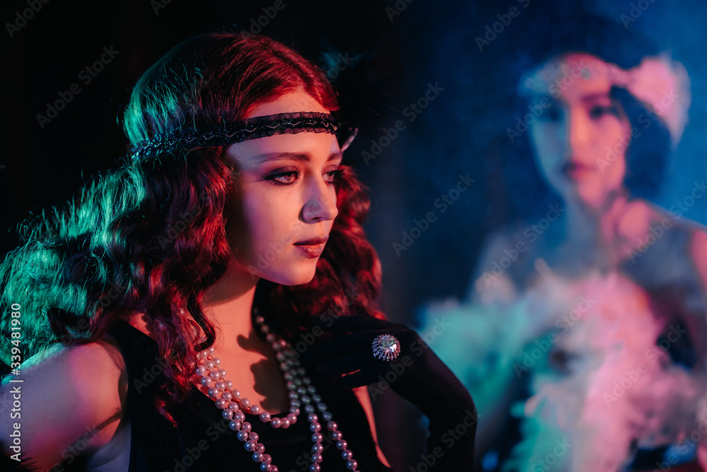 Portrait of young flapper women dressed in style of Great Gatsby posing on dark velours background. Roaring twenties, retro, party, fashion concept