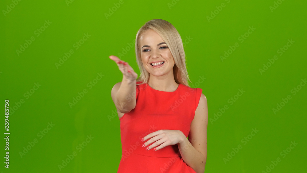 Fototapeta premium Lady in red on green screen background shows her hand looking at the camera