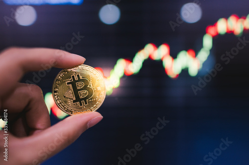 Bitcoins is virtual money. Gold bitcoins on hand with chart of growing and falling valuance of a cryptocurrency. Mining or blockchain technology.
