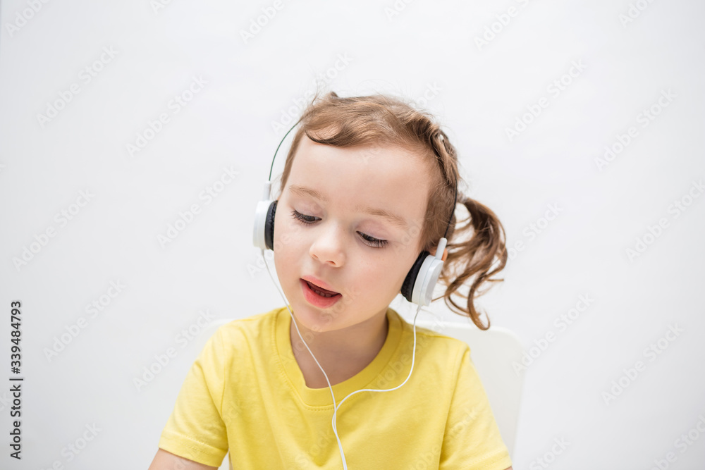 a girl on a white background in a yellow t-shirt. the little girl listens to music through headphones. a girl on a white background in a yellow t-shirt. the little girl listens to music through headphones.