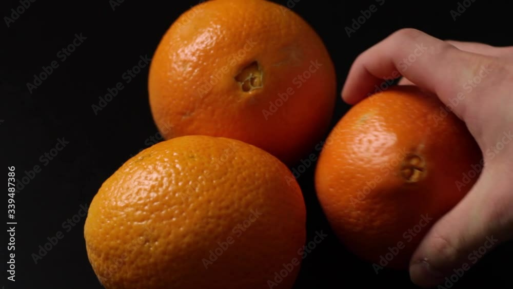 Caucasian hand puts three fresh whole fruit oranges on black isolated background Caucasian hand puts three fresh whole fruit oranges on black isolated background