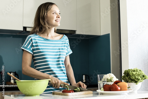 Closeup portrait of dreamy young beautiful woman slicing cucumber and cooking salad in kitchen. Healthy cooking concept.