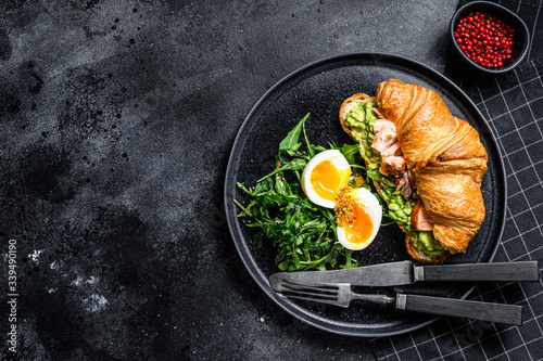 Breakfast, brunch croissant with hot smoked salmon, avacado. Garden green salad with arugula and egg. Black background. Top view. Space for text