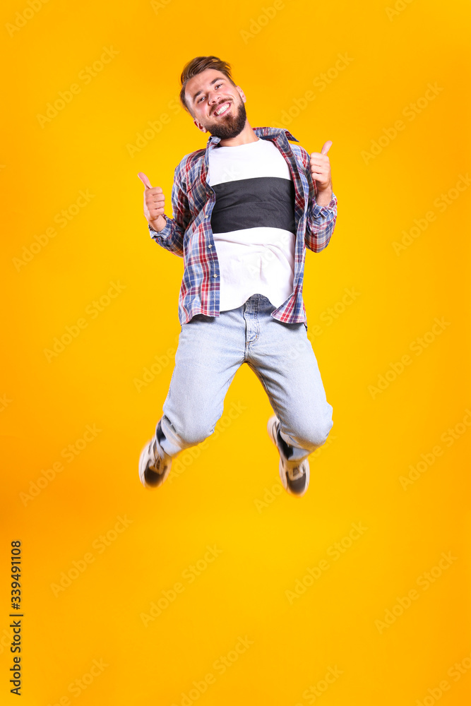 Young handsome man with facial hair jumping over yellow wall with a lot of copy space for text. Portrait of confident bearded male, wearing fashionable casual outfit. Isolated, background. Young handsome man with facial hair jumping over yellow wall with a lot of copy space for text. Portrait of confident bearded male, wearing fashionable casual outfit. Isolated, background.