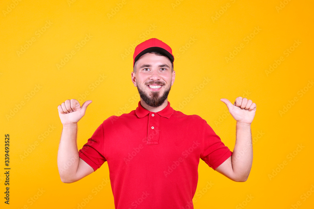 Young handsome delivery guy wearing red uniform and cap holding posing over isolated yellow background. Portrait of friendly bearded man in polo shirt and baseball hat. Copy space for text.