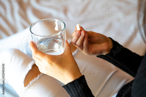 Close up of woman picking up a glass of water and a pill.