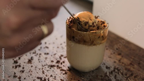 mixing the cremy Dalgona Coffee with a spoon, a trendy fluffy creamy whipped coffee with chocolate chips on a wooden table photo