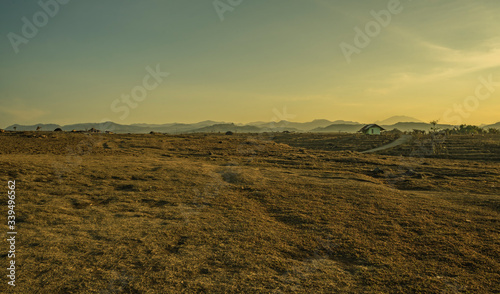 West Java dry countryside fields scene on yellow sunrise with mountains layers in distance. Haze bad visibility