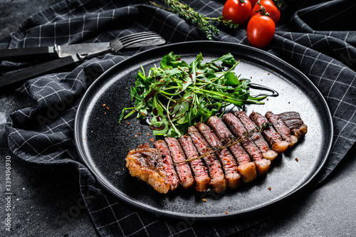 Cooked grilled strip loin steak, marbled beef meat with arugula. Black background. Top view