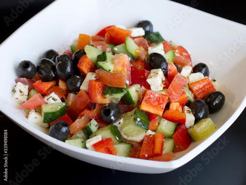 fresh greek salad in white plate on black table. vegetable salad with feta cheese. healthy food.