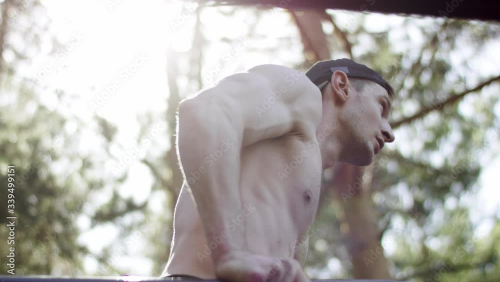 Adult caucasian athlete is doing push ups exercise on bars at the gym at the park topless during his daily workout, side close up shot Adult caucasian athlete is doing push ups exercise on bars at the gym at the park topless during his daily workout, side close up shot