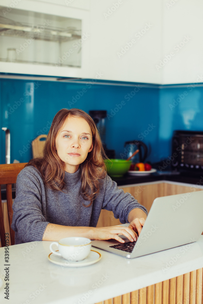 Closeup portrait of serious young beautiful woman drinking tea and working on laptop computer in kitchen. Freelancer concept. Closeup portrait of serious young beautiful woman drinking tea and working on laptop computer in kitchen. Freelancer concept.