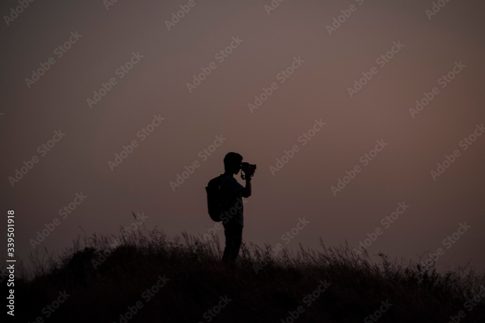 Men standing on hill photographing at sunset