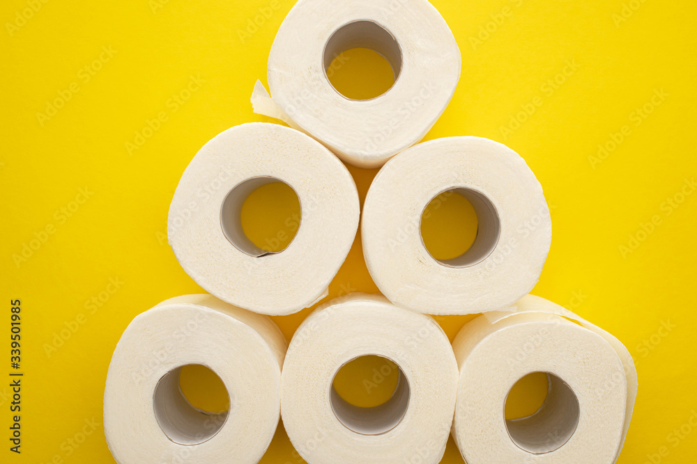 top view of white toilet paper rolls arranged in pyramid on yellow background top view of white toilet paper rolls arranged in pyramid on yellow background