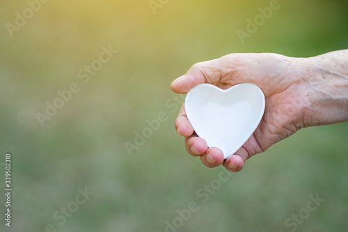 Close-up shot of a heart shaped white ceramic in the hand of an elderly woman. Valentine s day. Concept of people and health care