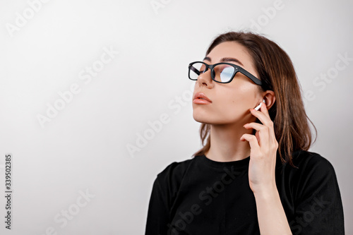 young brunette woman in a black t-shirt on a white background listens to music with glasses isolated