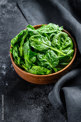 Young raw spinach in a wooden bowl. Black background. Top view