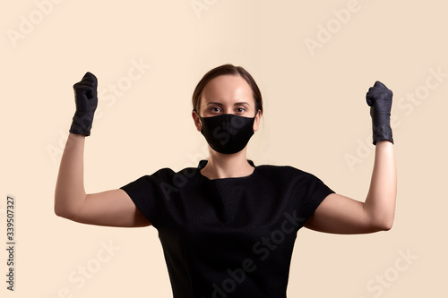 woman in black dress face mask and gloves raised her hands with fists and looking at camera