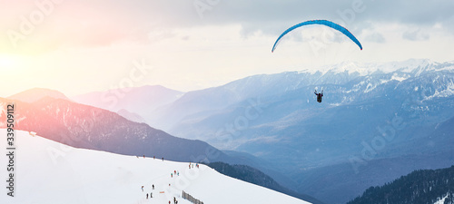 Banner. The landscape of the ski resort. Skiers and snowboarders are rolling down the mountain. paraglider flies over the valley. Mountains of Sochi Krasnaya Polyana, Russia. Place for text.
