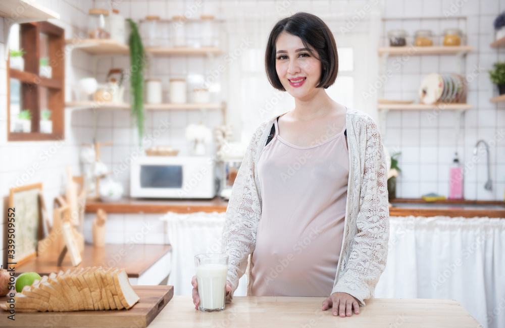 Portrait beautiful young asian pregnant woman drink milk glass standing in kitchen at home.Health care and love of pregnancy mother’s day concept. Portrait beautiful young asian pregnant woman drink milk glass standing in kitchen at home.Health care and love of pregnancy mother’s day concept.