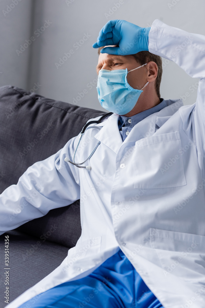 tired and mature doctor in medical mask sitting on sofa tired and mature doctor in medical mask sitting on sofa
