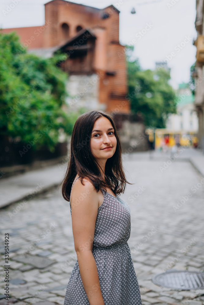 Fototapeta premium Smiling beautiful girl walking in the city. Brunette girl in summer dress on city tour.