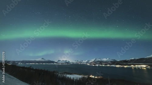 Green Northern Lights on Night Sky with Stars and Snowy Mountains at Winter Night. Balsfjorden, Troms, Norway. Time Lapse photo