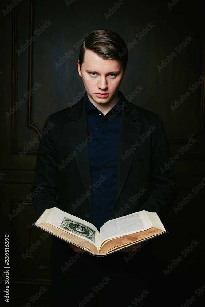 Handsome young man in a black shirt and with trendy hairdo, holding ancient book posing on a dark studio background.
Handsome young man in a black shirt and with trendy hairdo, holding ancient book posing on a dark studio background.