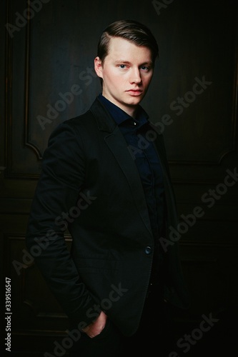 Handsome young man in a black shirt and with trendy hairdo posing on a dark studio background.