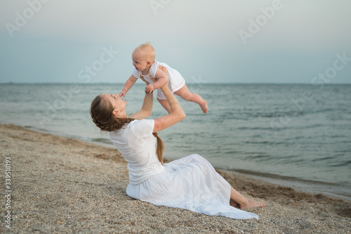 Cuadro en lienzo Mother throwing baby up on sandy beach sea background