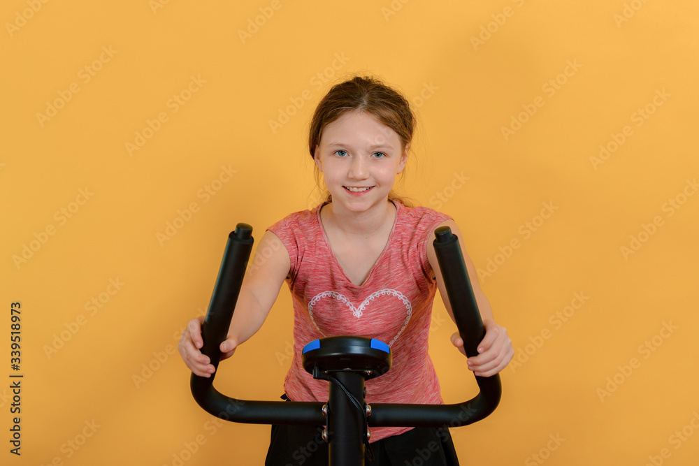 The girl goes in for sports, the child on a stationary bike does cardio and looks forward to the camera. The girl goes in for sports, the child on a stationary bike does cardio and looks forward to the camera.