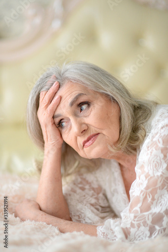 Close up portrait of sad senior woman lying on bed