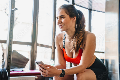 Portrait of joyful young sportswoman sitting and using cellphone Free Download Portrait of joyful young sportswoman sitting and using cellphone - GFXLoad