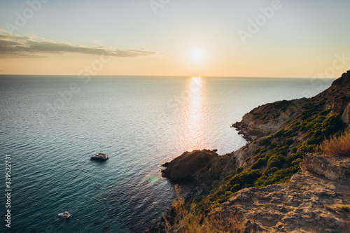 beautiful sunset view from the cliff by the blue sea with two boats off the coast.