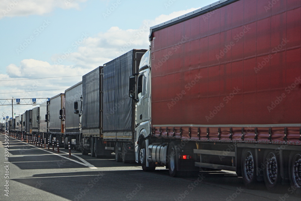 Large endless queue of trucks with semi trailers to the control point in the spring against the blue sky,