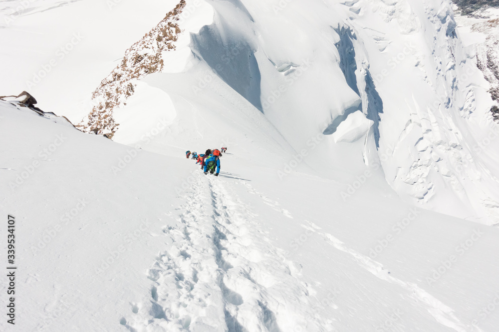 Group of mountaineers climbing a very steep slope of snow near the summit of Liskamm, between Italian and Swiss Alps