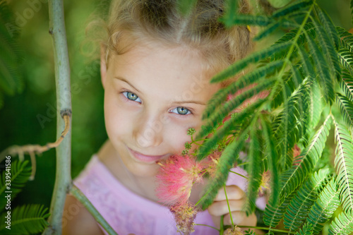 Close-up portrait of a child. Summer funny little girl next to a pink acacia in bloom. Albizia julibrissin