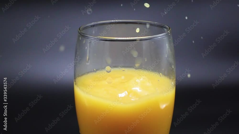 Pieces of ice fall in a glass with orange juice on a black background. Slow Motion 500 FPS Pieces of ice fall in a glass with orange juice on a black background. Slow Motion 500 FPS