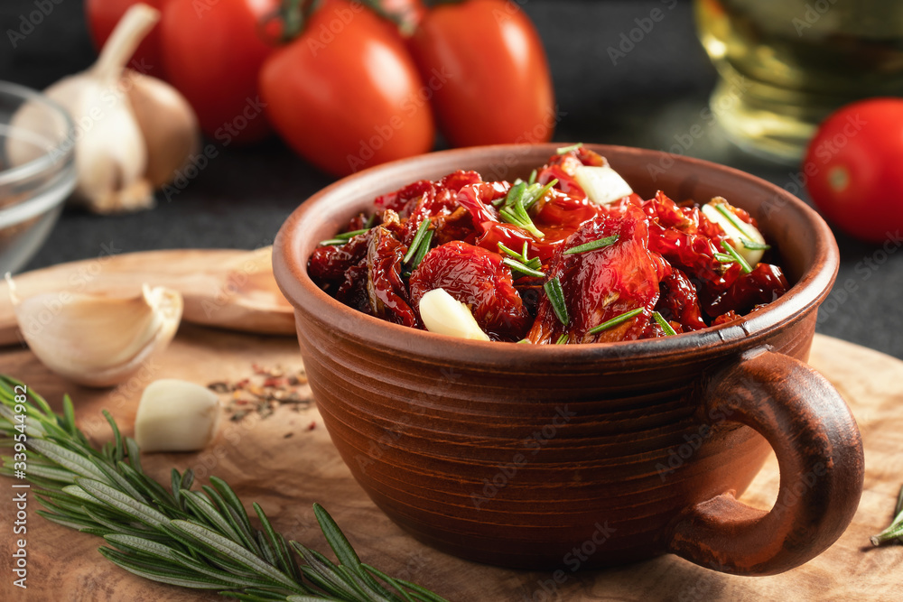 Sun-dried tomatoes with garlic, rosemary and spices in a clay bowl on an olive wood cutting board Sun-dried tomatoes with garlic, rosemary and spices in a clay bowl on an olive wood cutting board