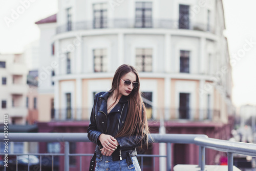 beautiful brunette lady wearing glasses and a leather jacket on a background of city