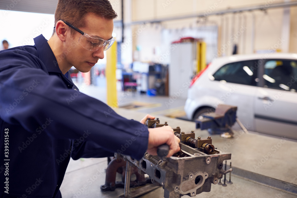 Female Student Works On Car Engine Block On Auto Mechanic Apprenticeship Course At College Female Student Works On Car Engine Block On Auto Mechanic Apprenticeship Course At College