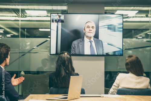 Employees listening to mature leader during video conference. Business people looking at monitor screen during video conference in office. Business conference concept