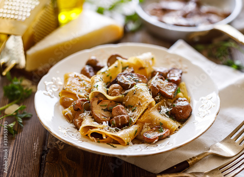 Pappardelle pasta with porcini mushrooms, sprinkled with parmesan cheese and chopped parsley in a ceramic plate on a wooden table, close up.  photo