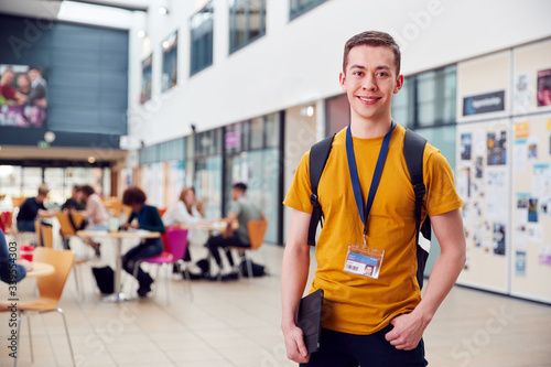 Portrait Of Smiling Male College Student In Busy Communal Campus Building