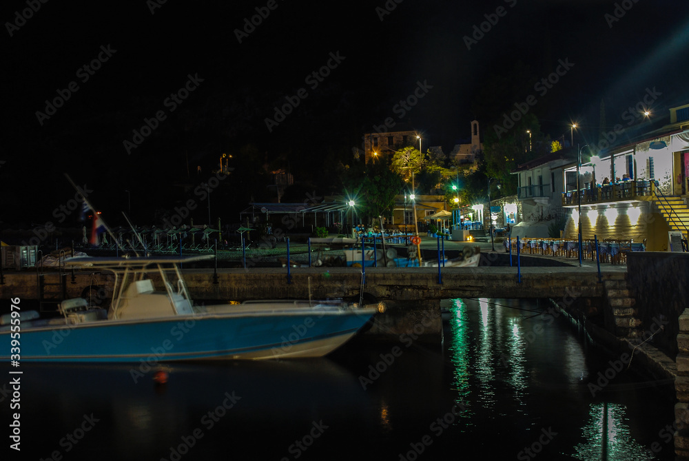 Evening in the picturesque sea bay. Beautiful beach with restaurants and boats. Bright lighting reflected in calm water.